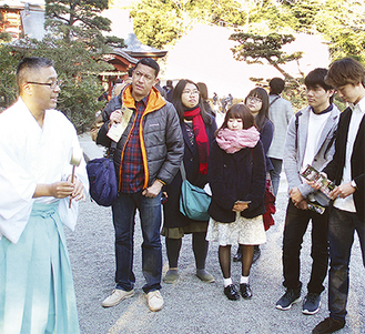 鶴岡八幡宮で神職の話を聞く留学生と現役学生（同会提供）