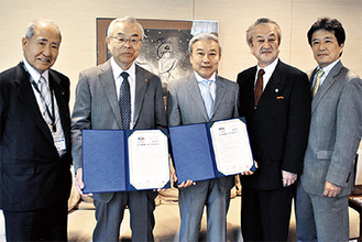 協定書を手にする塩野院長（左から２人目）と鶴岡会長（中央）
