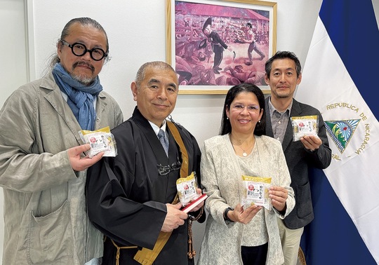 「御難おむすび」を持つ、（左から）澤渡さん、平井住職、サンディ・ダビラ大使、増山さん