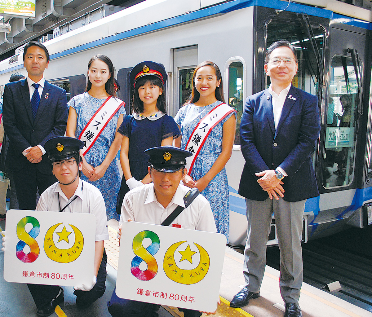 記念ロゴを持つ運転士と車掌、石井さん(後列中央)ら