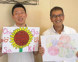 優秀賞の作品を手にする小林会長（右）と鈴木副会長左が秋元美玖さんの作品、右が須崎勇太くんの作品