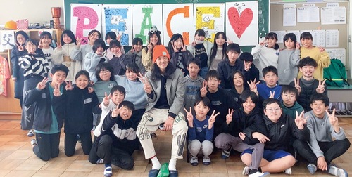 完成したデザインの前で写真を撮るアンベさんと児童