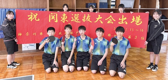 関東大会に出場する男子卓球部（前列）。女子卓球部のメンバーは、美術部が制作した横断幕を持ちエールを送る
