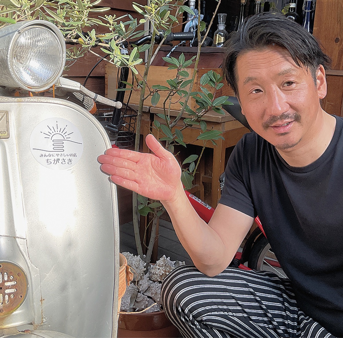 店舗前に掲示したステッカーを指さす八木さん
