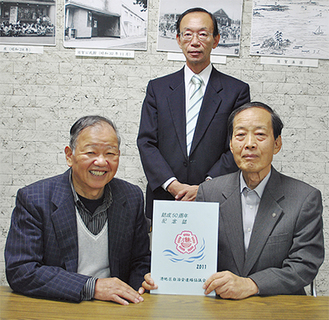 50周年記念誌を手にする編集委員長の清田さん（右）と府川さん（左）、冨田さん（後ろ）