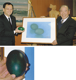 （上）卵を手にする落合克宏市長と絵画を手に笑顔の原安雄会長（左）深い緑色の厚い殻に覆われたエミューの卵