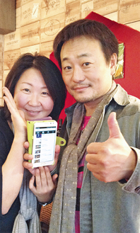 開発したアプリ画面を持つ同団体メンバーと川村代表（右）