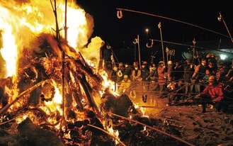 燃え盛る炎に団子を括り付けた竹竿を伸ばす参加者（昨年）