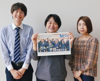 受賞した広報紙を手に喜びを語る三澤さん（中央）と広報紙を作成している職員