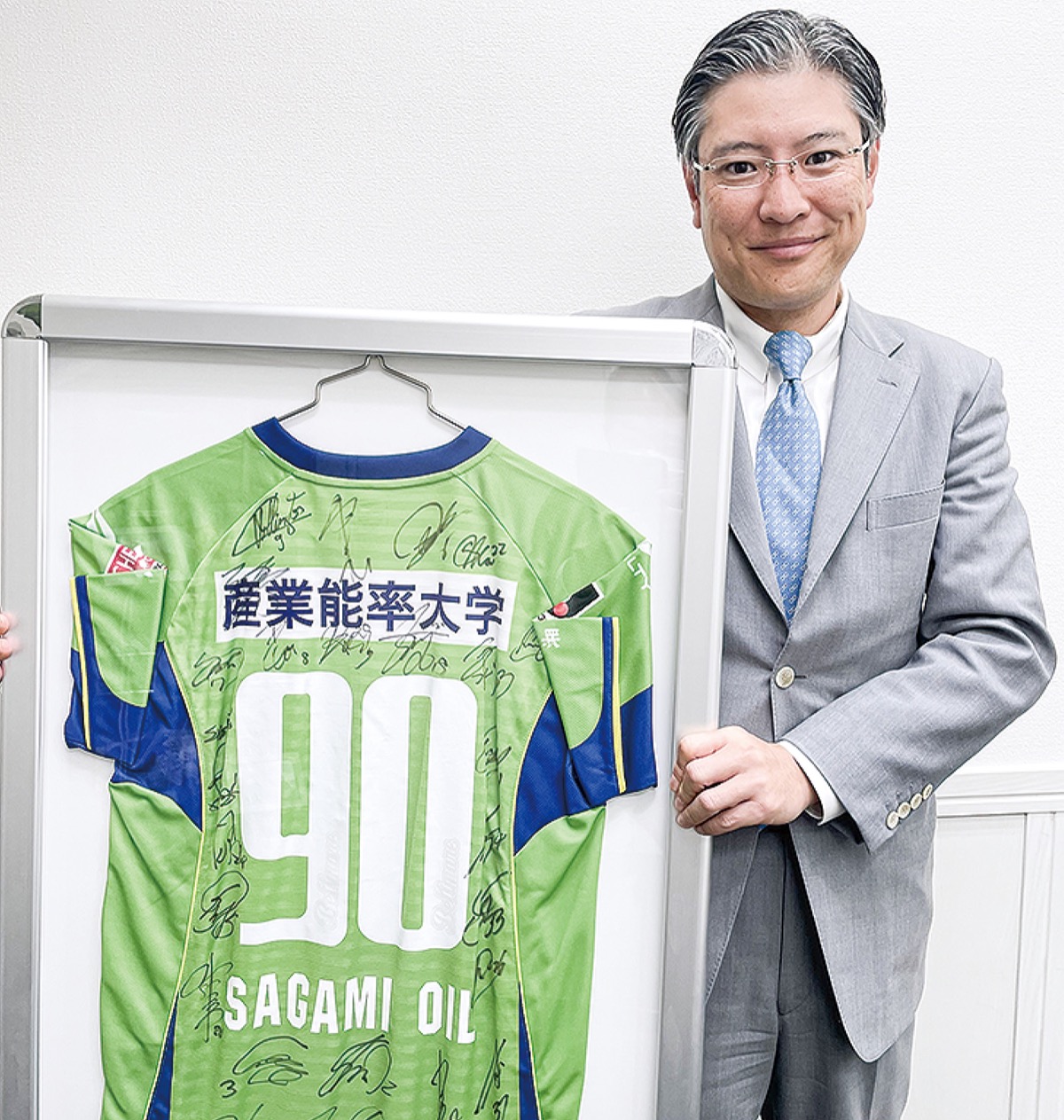 創業90周年の時に湘南ベルマーレから寄贈された選手のサイン入りユニホームを持つ小泉代表