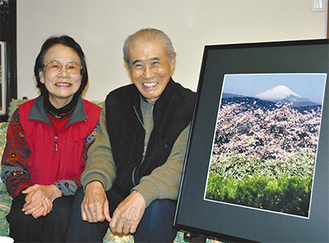 地元で初の写真展を開催する白崎裕彦さんと広子さん。右側は二宮の吾妻山で撮影した富士と桜・雪柳・菜の花の写真。「広報にのみや」の表紙に採用された