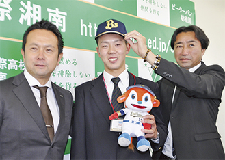中川アマチュアスカウトグループ長（右）から帽子を被せてもらう本田投手。左は由田スカウト