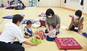 母子保健コーディネーターが見守る中、広間で遊ぶ親子