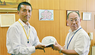 栁下校長（右）にヘルメットを手渡す小林会長（左）