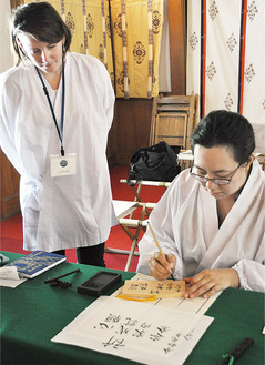 絵馬に筆で願い事を書く姿を見守る佐々木さん（左）