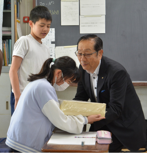 児童に現金見本を渡す本多会長（右）