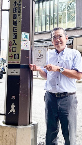 柱に張られたステッカーとORE登録証を持つ穂坂会長