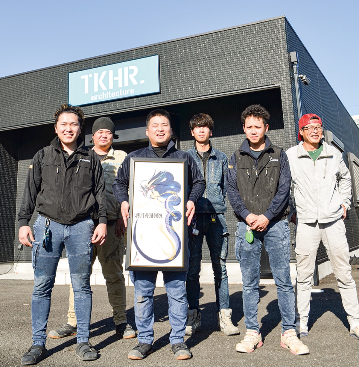 竜の絵が描かれた作品を持つ内田さんを中心に同社の若手社員たち