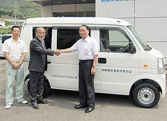 納車した軽自動車の前で握手をかわす佐藤ＬＣ会長（中央）と上田会長（右）。左は湯川嘉一ＬＣ薬害広報委員長。