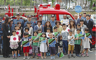 両国の国旗を持つ子どもたちが消防自動車の前で記念撮影