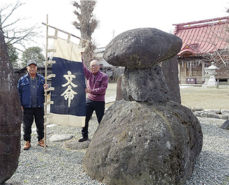 麻を藍で染めた「のぼり旗」を持つ山口冨美男さん（左）と大脇良夫さん（右）石碑は文命東堤碑（左）と文命宮（右）＝福沢神社