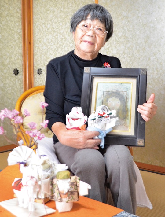自身の和紙人形と亡夫の油絵を持つ露木さん
