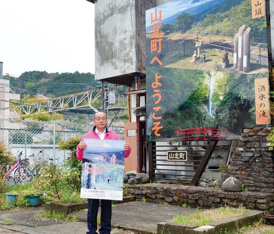 看板の前でポスターを手にする佐藤事務局長