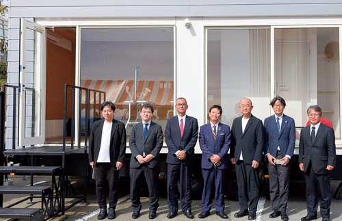 トレーラーハウスの前で記念撮影する関係者ら