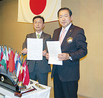 阿蘇会長（右）と斎藤会長の間で仮調印が執り行われた