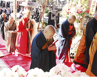 朱色の法衣をまとい、僧侶とともに本堂に入る船越寿光住職
