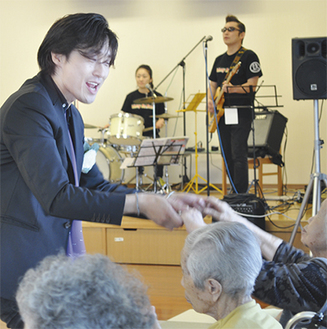 車いすに乗ったお年寄りの手を握り、演奏に合わせて一緒にダンスを踊るケンイチ大倉さん（左）