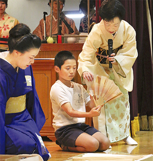 岩井会長（右）から扇子の開き方を教わる児童