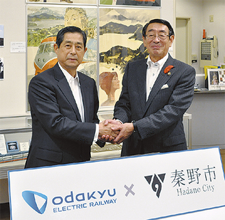 観光ポスターなどが展示された小田急コーナーの前で握手する山木社長（左）と古谷市長