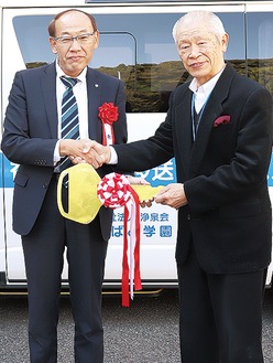 贈呈式が行われ、西田理事長（右）に模造キーが手渡された。バックは寄贈された車両