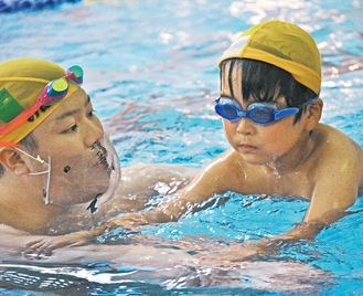 コーチの腕につかまり泳ぎ方を教わる児童