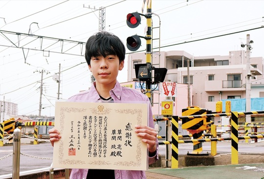 感謝状を手にする草間さんとエスコートゾーンが設置される予定の鶴巻温泉駅横の踏切