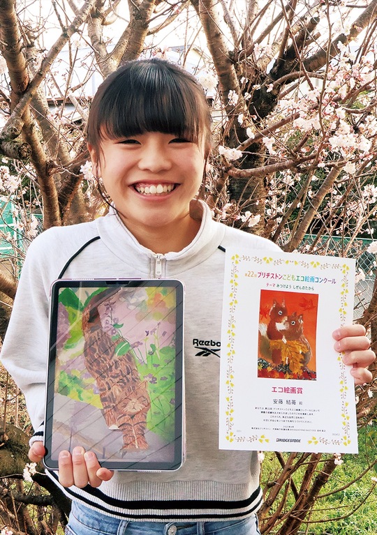 カナガワビエンナーレで特別賞を受賞した作品（左・事前撮影した作品の写真）とエコ絵画コンクールでの賞状（右）を持つ安藤さん